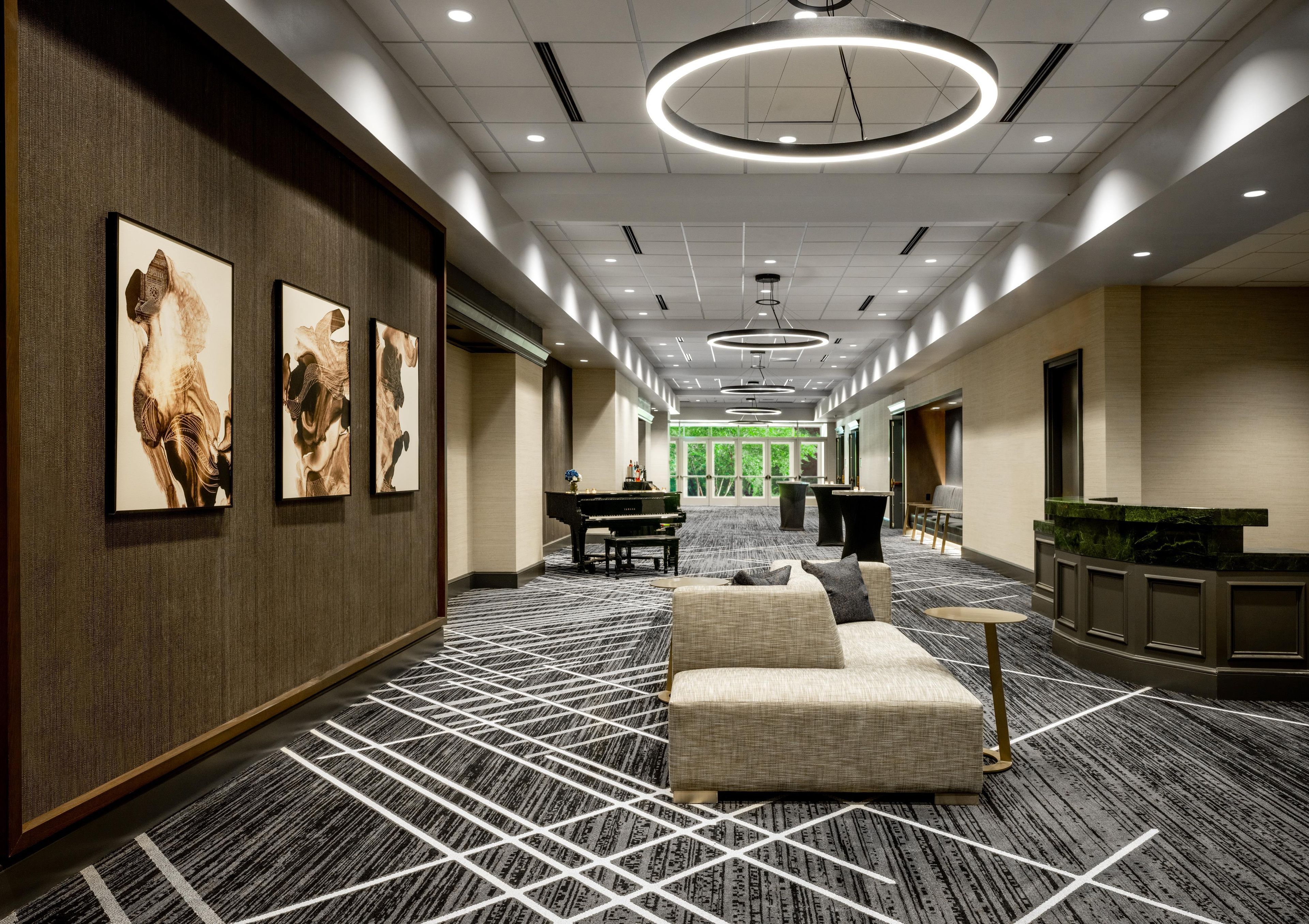 Um hall de hotel com um piano de cauda, área de estar e obras de arte nas paredes.