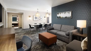 A hotel room with a dining area, a sofa, an ottoman, and a TV.