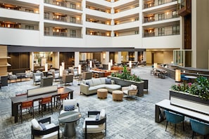 Un hall d’hôtel à plusieurs niveaux, doté d’espaces de détente, de tables et d’un arrangement floral central.