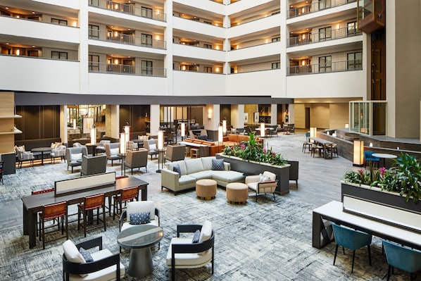 Un hall de hotel de varios niveles con zonas de estar, mesas y un arreglo floral central.