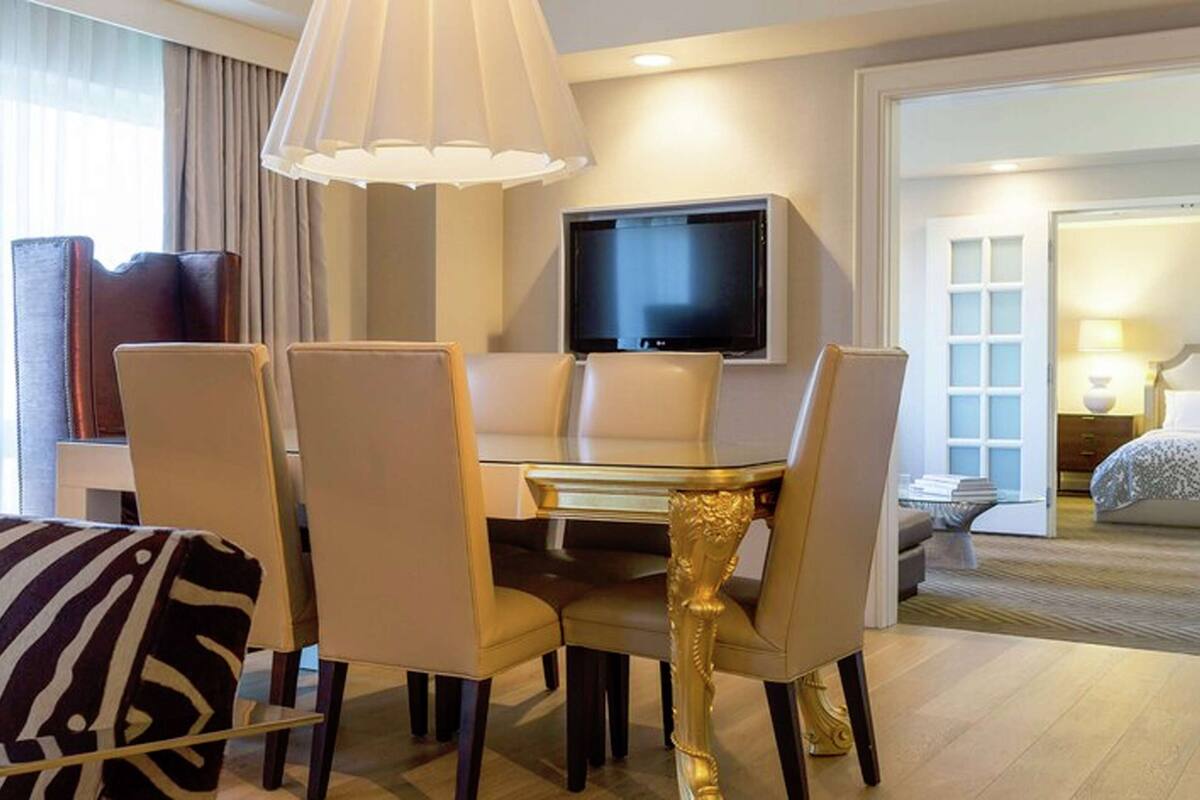 Une chambre d’hôtel comprenant un coin repas avec une table et des chaises, un téléviseur et un lit avec une table de chevet.