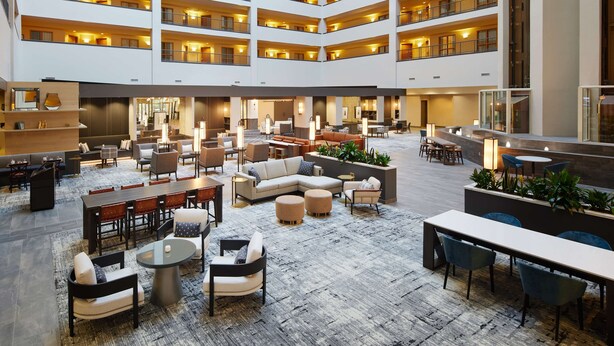 Eine mehrstöckige Hotelhalle mit einem zentralen, offenen Bereich, mehreren Sitzgruppen und unterschiedlichen Tischen und Stühlen.
