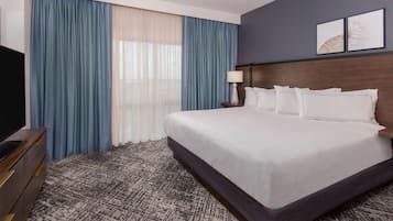 A hotel room with a large bed, a TV, a nightstand, and a window with curtains.