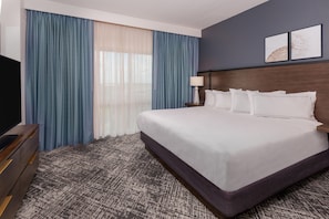 Een hotelkamer met een groot bed, een televisie, een nachtkastje en een raam met gordijnen.