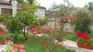 Un jardín con diversas plantas florecientes y un edificio de piedra con techo de tejas.