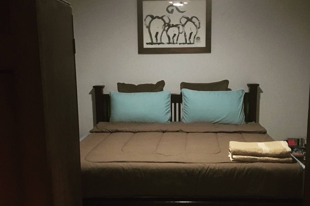 A bedroom with a bed, two pillows, a blanket, and a framed artwork on the wall.