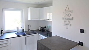 Una cocina moderna con armarios blancos, encimera gris y un pequeño comedor con una mesa y una silla grises.