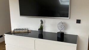 Una sala de estar moderna con un televisor de pantalla plana grande montado en una pared blanca, un mueble blanco debajo y una pequeña planta en maceta sobre el mueble.