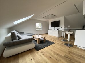 A modern living room with a sectional sofa, a coffee table, and a TV mounted on the wall. - Uraha Apartments (Herzogenaurach)