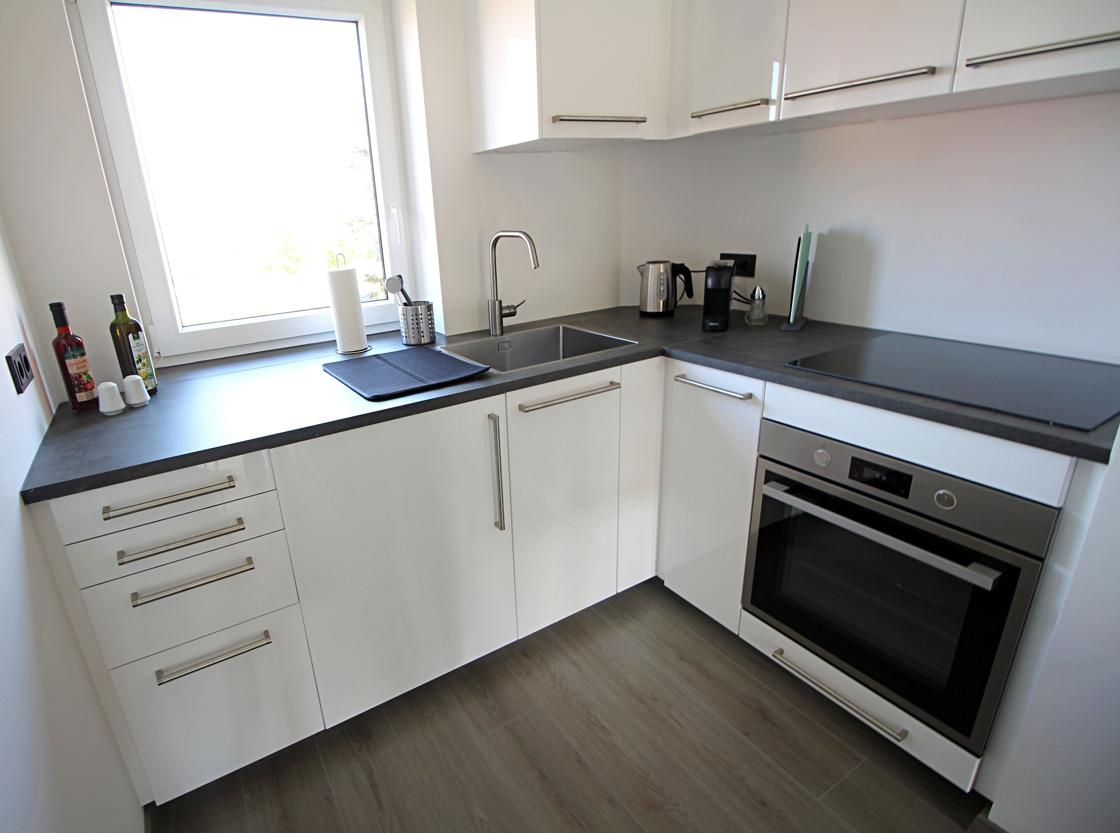 A modern kitchen with white cabinets, a black countertop, a stainless steel sink, and a built-in oven.