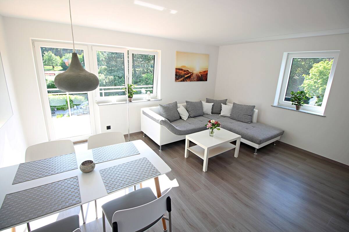 Una sala de estar moderna con un sofá, una mesa de comedor y dos ventanas.