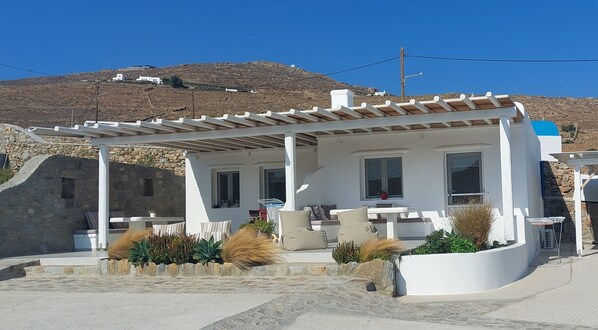 A white villa with a covered patio, stone walls, and a view of a mountainous landscape.