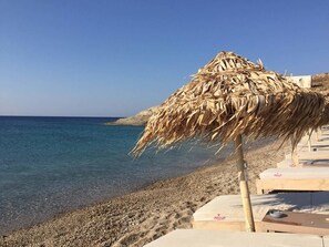 A beach with a thatched umbrella, lounge chairs, and a pebble beach.