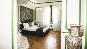 A hotel room with a bed, a nightstand, a dresser, a window with curtains, and a decorative vase.