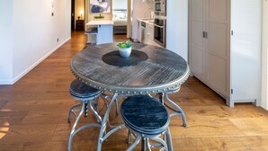 A modern kitchen with white cabinets, stainless steel appliances, and a round dining table with stools. - Jukebox Lofty Views-Perfect Mix of Indoor / Outdoor Living, Gym and Free Parking by Victoria Prime! (Victoria)