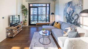 A modern living room with a large window, a sofa, a coffee table, and a television on a wooden stand. - Jukebox Lofty Views-Perfect Mix of Indoor / Outdoor Living, Gym and Free Parking by Victoria Prime! (Victoria)