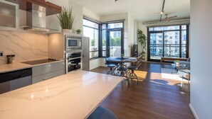A modern kitchen with a marble countertop, built-in appliances, and a dining area with a round table and chairs. - Jukebox Lofty Views-Perfect Mix of Indoor / Outdoor Living, Gym and Free Parking by Victoria Prime! (Victoria)