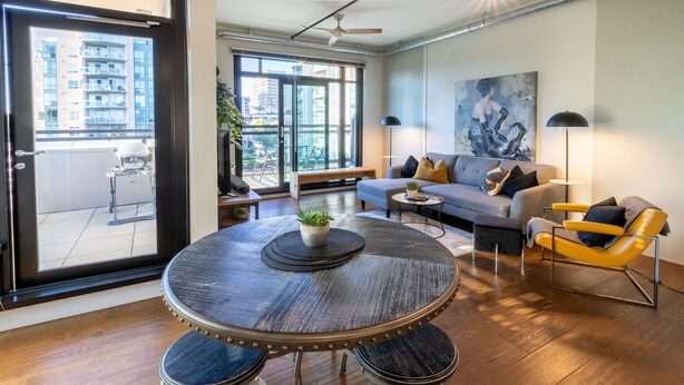 A modern living room with a round dining table, a sofa, and a yellow chair. - Jukebox Lofty Views-Perfect Mix of Indoor / Outdoor Living, Gym and Free Parking by Victoria Prime! (Victoria)