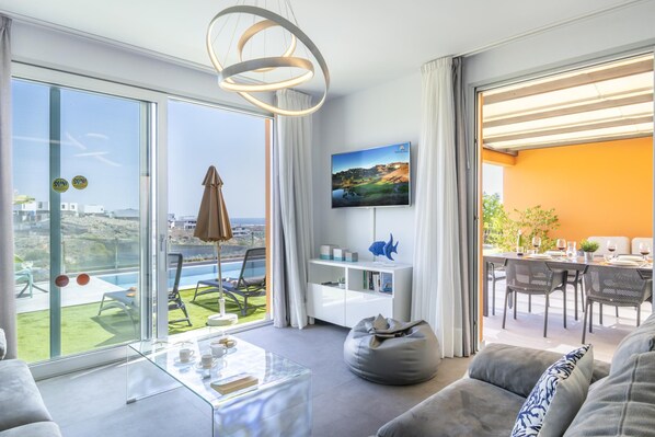 A modern living room with a glass wall, a dining area, and a view of the landscape.