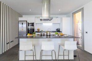 A modern kitchen with a central island, stainless steel appliances, and white bar stools.