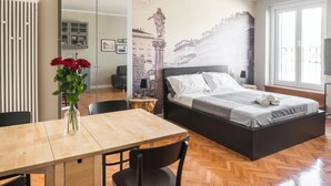 A bedroom with a bed, a wooden table, chairs, a vase with flowers, and a mural on the wall. - Al Garibaldino Rooms (Trieste)