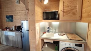Cozinha compacta com paredes de madeira, micro-ondas, pia, máquina de lavar e frigorífico.
