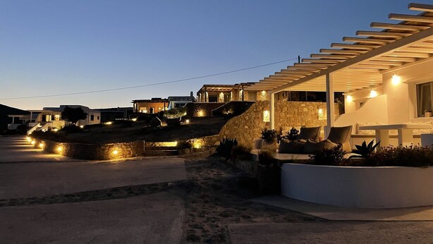 Una casa moderna con fachada de piedra, un área de estar cubierta al aire libre y un camino de entrada bien iluminado.