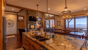 A spacious kitchen with a large island, wooden cabinets, and a stone fireplace. - Whitetail Ridge Lodge - Eagles Nest, long range views, three masters (Banner Elk)