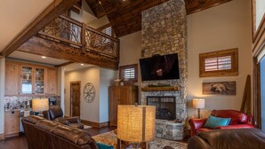 A spacious living area with a stone fireplace, leather sofas, and a high ceiling with exposed beams. - Whitetail Ridge Lodge - Eagles Nest, long range views, three masters (Banner Elk)