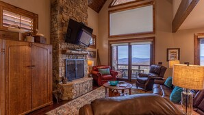 A cozy living room with a stone fireplace, leather furniture, and a large window offering a mountain view. - Whitetail Ridge Lodge - Eagles Nest, long range views, three masters (Banner Elk)