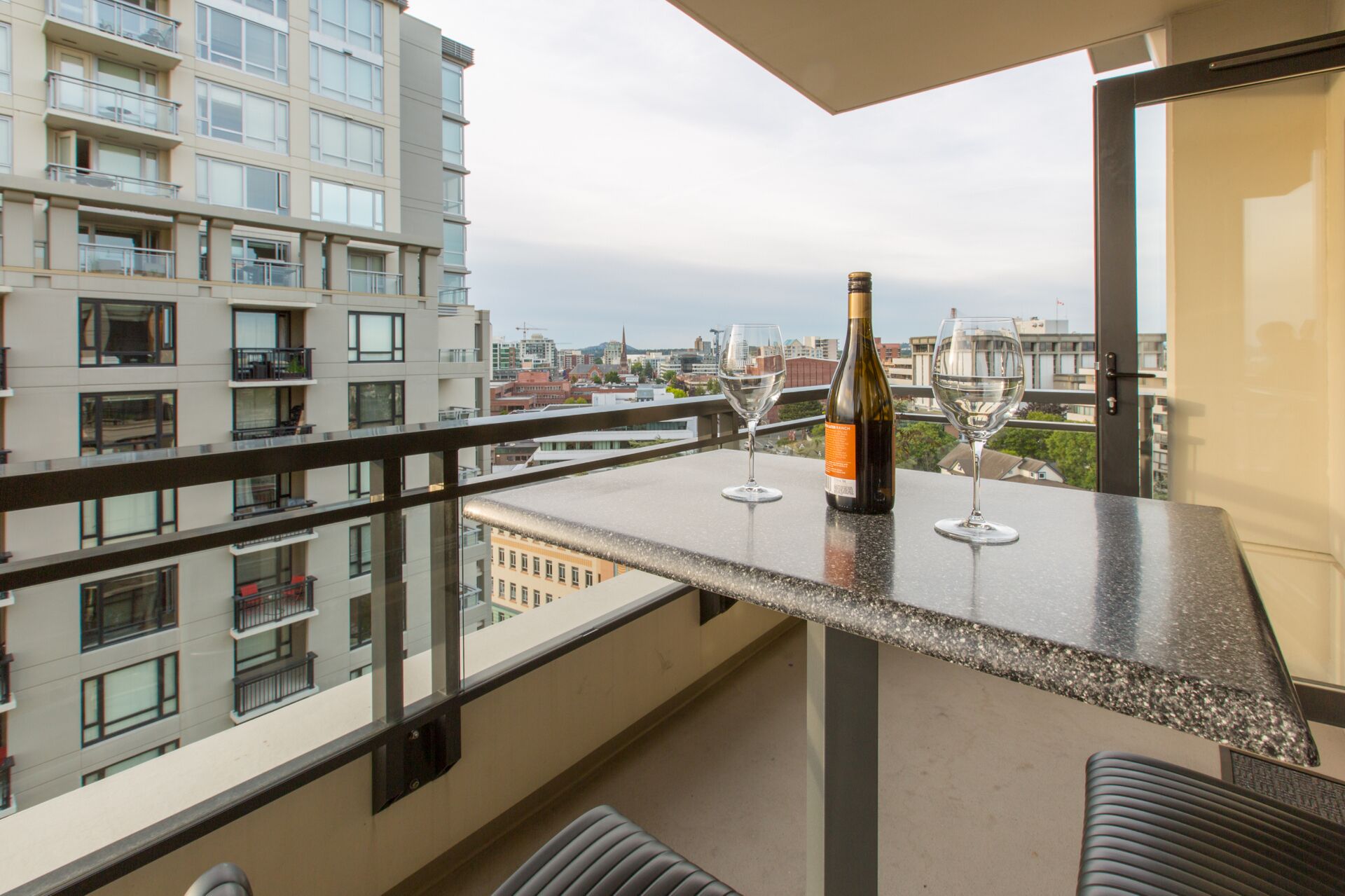 Un balcon avec une table, deux verres à vin et une bouteille de vin.