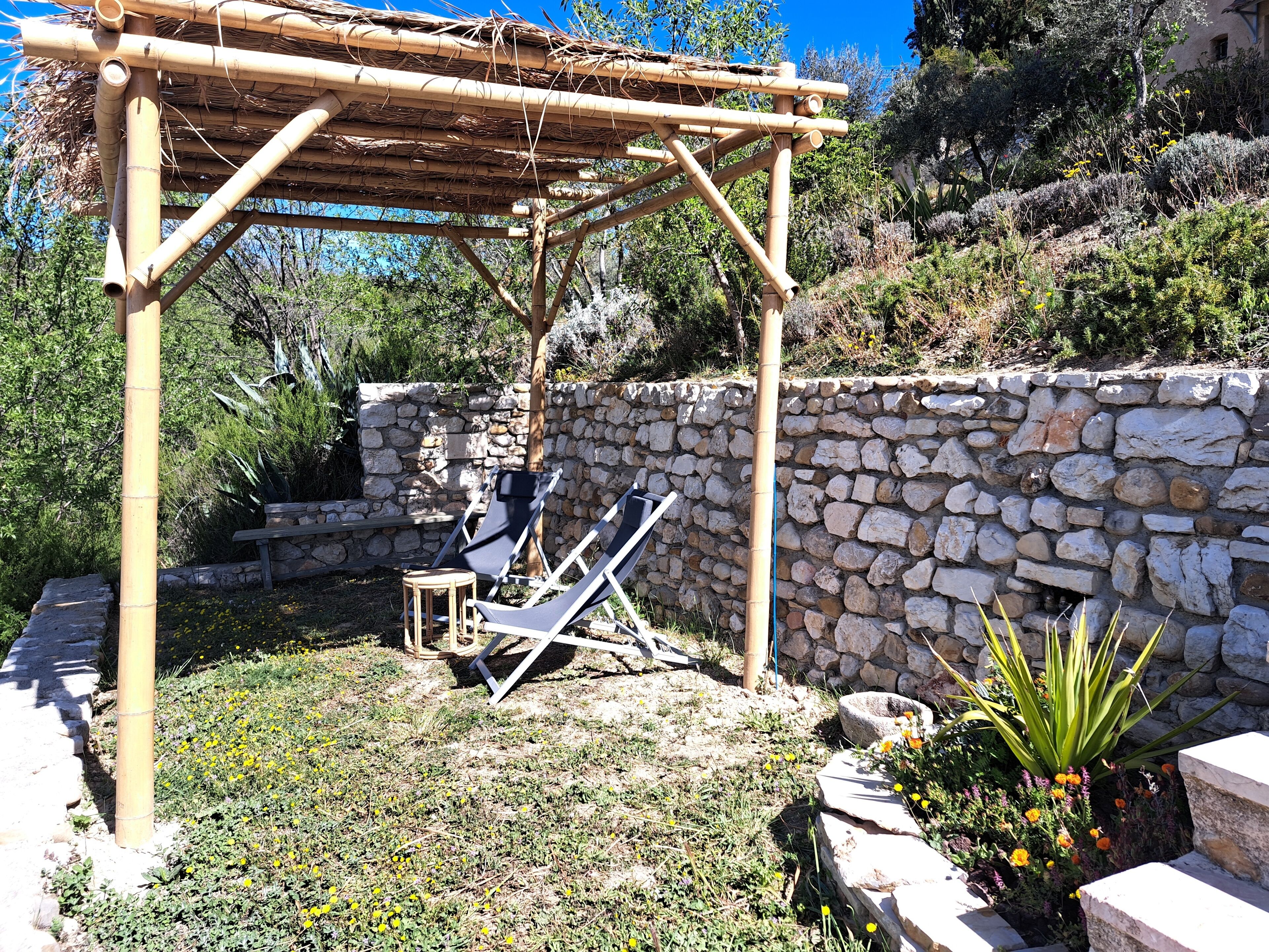 Eine Steinsäule mit einer Pergola, zwei Liegestühle und einem kleinen Tisch.