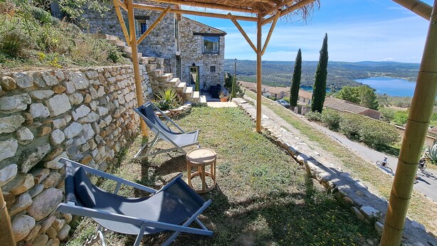 Een stenen huis met een pergola en lounge stoelen.