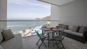 Un balcon avec vue sur l’océan et une piscine. On y trouve une table à manger avec des chaises et un canapé.