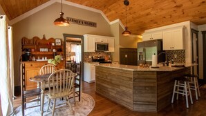 A kitchen with wooden ceiling, white cabinets, a central island, bar stools, and a sign reading "FARMER'S MARKET".