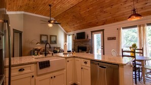 A kitchen with white cabinets, a dishwasher, a granite countertop, a ceiling fan, and a fireplace.