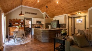 A cozy kitchen with wooden ceiling, a dining area with a round table and chairs, and a living room with a sofa and a globe on a side table.