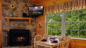 A cozy room with a stone fireplace, a television mounted above it, and a dining table set for two. - Hot Tub& Mountain Views - Min to National Park! (Sevierville)