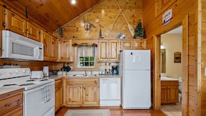 A wooden cabin kitchen with a stove, microwave, refrigerator, and wooden cabinets. - Hot Tub& Mountain Views - Min to National Park! (Sevierville)
