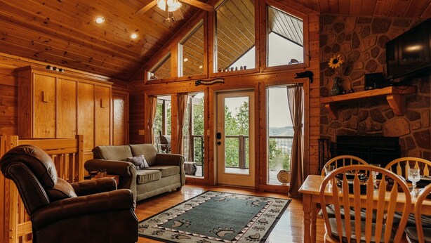A cozy cabin interior with a fireplace, wooden furniture, and large windows. - Hot Tub& Mountain Views - Min to National Park! (Sevierville)