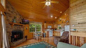 A cozy cabin interior with a stone fireplace, wooden ceiling, and a dining area with a table and chairs. - Hot Tub& Mountain Views - Min to National Park! (Sevierville)