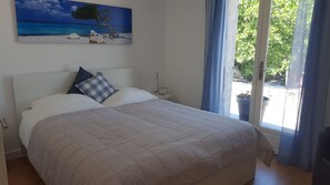 A bedroom with a bed, a nightstand, a clock, and a window with curtains. - Villa des Lunes in the center of Le Plan de la Tour with heated swimming pool and large garden (Le Plan-de-la-Tour)