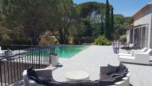 Zona de piscina con mobiliario, una piscina y vegetación circundante.