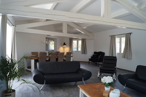 Un vaste espace de vie doté d’un plafond haut, d’une table à manger avec des chaises, d’un canapé et d’un piano.