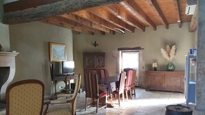 A rustic room with exposed wooden beams, a dining table with chairs, a television, and a cabinet. - Character cottage near Verdun (Dieue-sur-Meuse)
