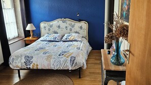 A bedroom with a bed, a wooden floor, a blue wall, a hanging lamp, and a vase with dried flowers. - Character cottage near Verdun (Dieue-sur-Meuse)