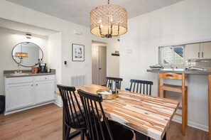 A modern kitchen with white cabinets, a wooden dining table, and a hanging light fixture.