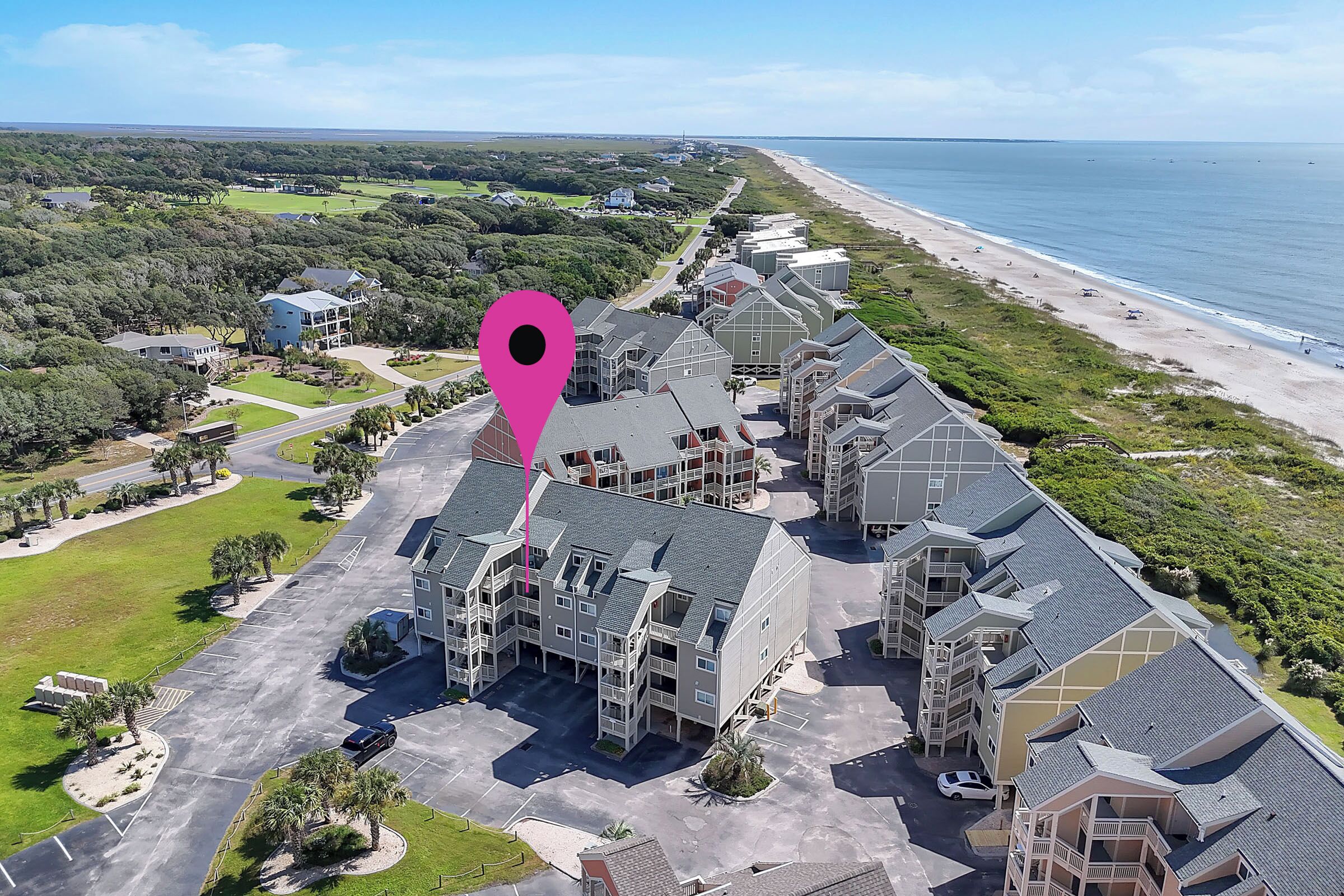 A residential complex with multiple buildings, a parking area, and a beach view.
