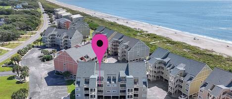 Vue aérienne d’un hôtel situé sur la côte, composé de plusieurs bâtiments, avec un parking et une plage en arrière-plan.