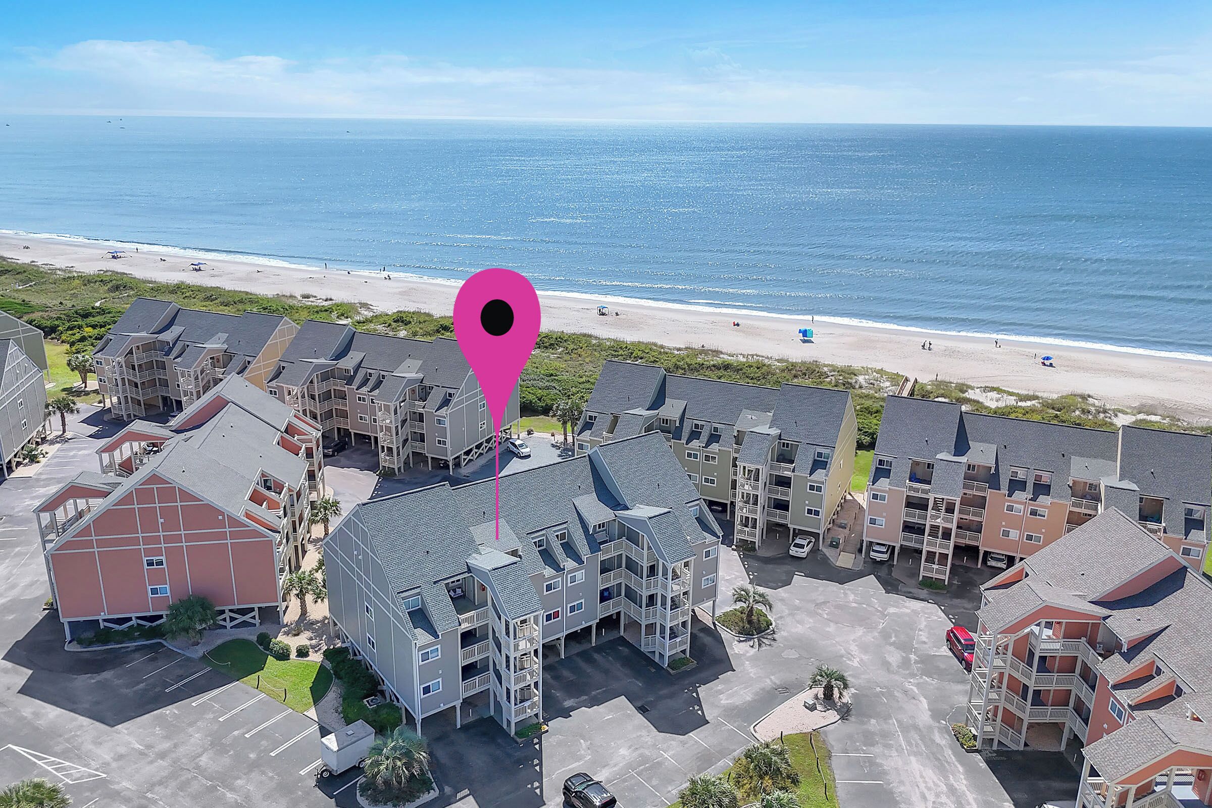 An aerial view of a residential area with multi-story buildings, a parking lot, and a beach in the background.